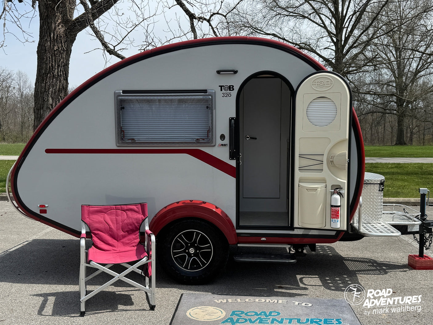 This T@B 320 teardrop RV rental, white with red trim, is parked outside with a camping chair, ready for adventure.