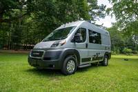 A silver camper van, an excellent RV rental choice, is parked on lush green grass with trees in the background, ready for travel. — photo 3
