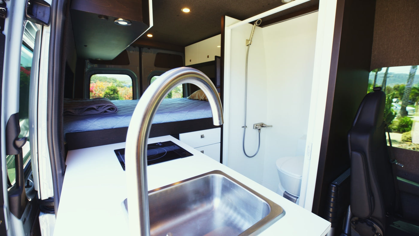 Cozy RV rental interior featuring a compact kitchen with sink/stove, rear bed, and small shower/toilet area. Perfect for travel! — photo 8