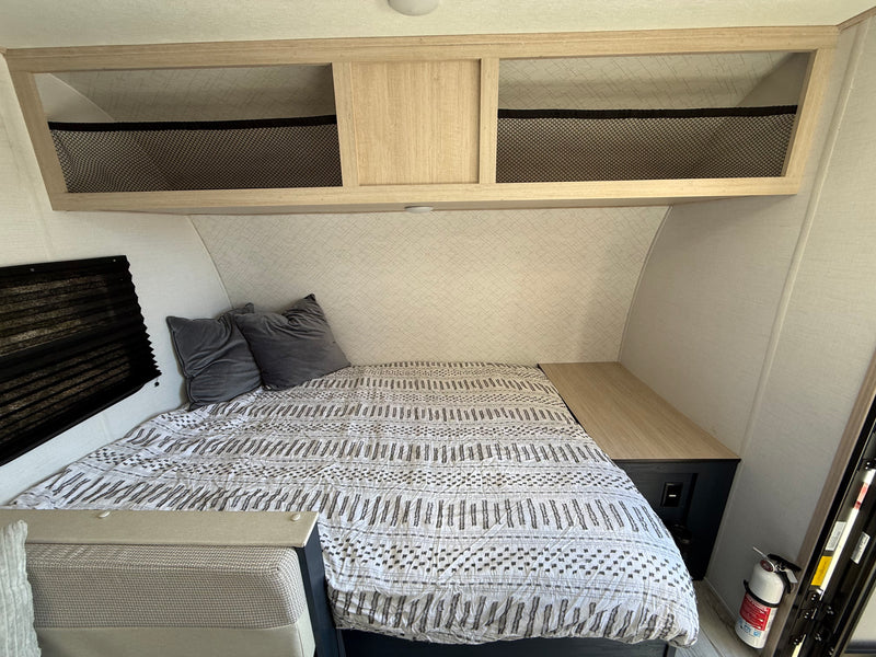 Cozy RV rental bedroom with a comfortable bed, patterned comforter, overhead storage, and bedside shelf. — photo 15