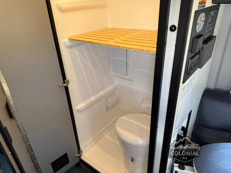 This rv rental shows a compact bathroom with a toilet, shower area, and a wooden shelf, perfect for small spaces.