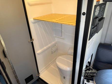 This rv rental shows a compact bathroom with a toilet, shower area, and a wooden shelf, perfect for small spaces.