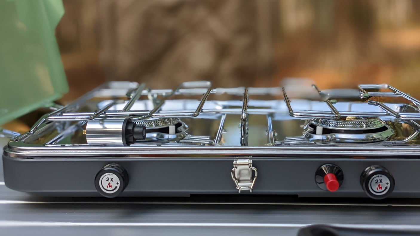 A compact, dark grey two-burner camping stove with chrome grates, ideal for an RV rental trip's outdoor cooking needs.