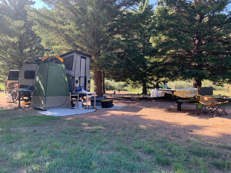 Relaxing RV rental campsite. Features a pop-up trailer with a privacy tent, picnic table, and chairs shaded by tall trees. — photo 4