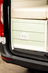 Custom RV rental interior: light green shiplap wall, white electrical outlet, and a beige cushion.