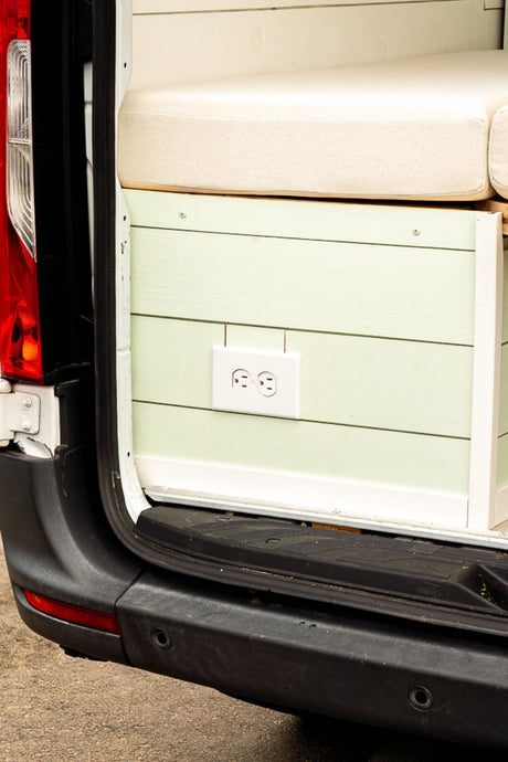 Custom RV rental interior: light green shiplap wall, white electrical outlet, and a beige cushion.