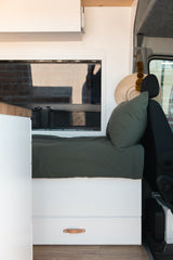 Modern RV rental interior: green bed, storage drawer with leather pull, and scenic window reflections.