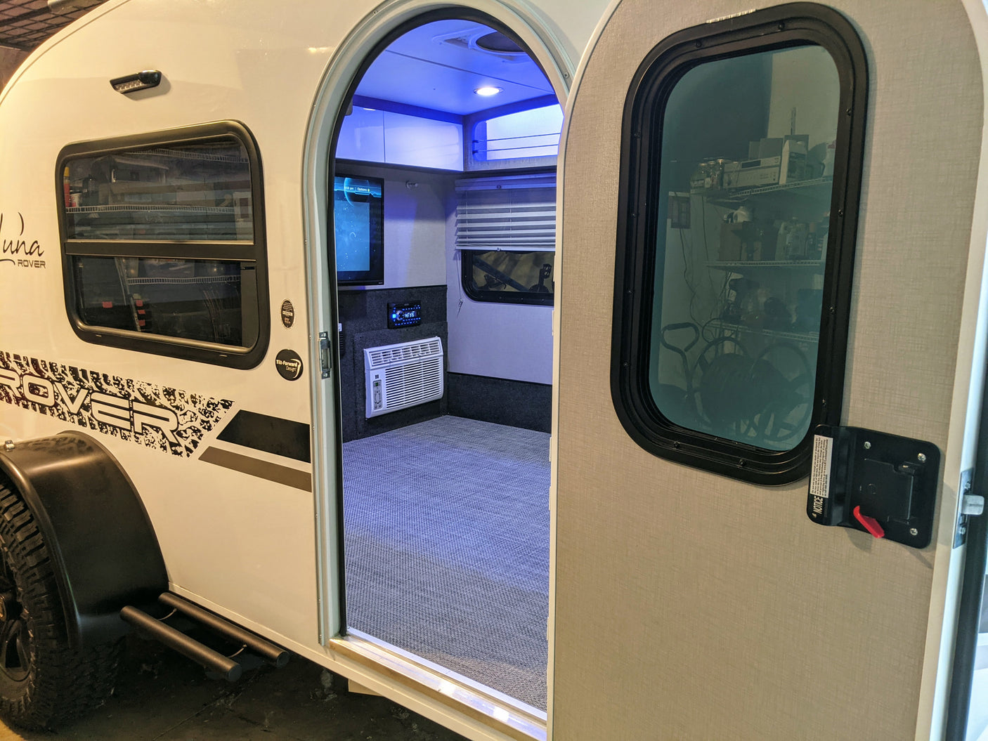 An open door reveals the comfy interior of this modern RV rental. Features include AC, TV, and blue mood lighting, ideal for travel.