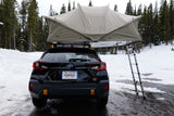 Rear view of a black Subaru with a large rooftop tent and ladder, parked in snow, resembling an RV rental for camping.