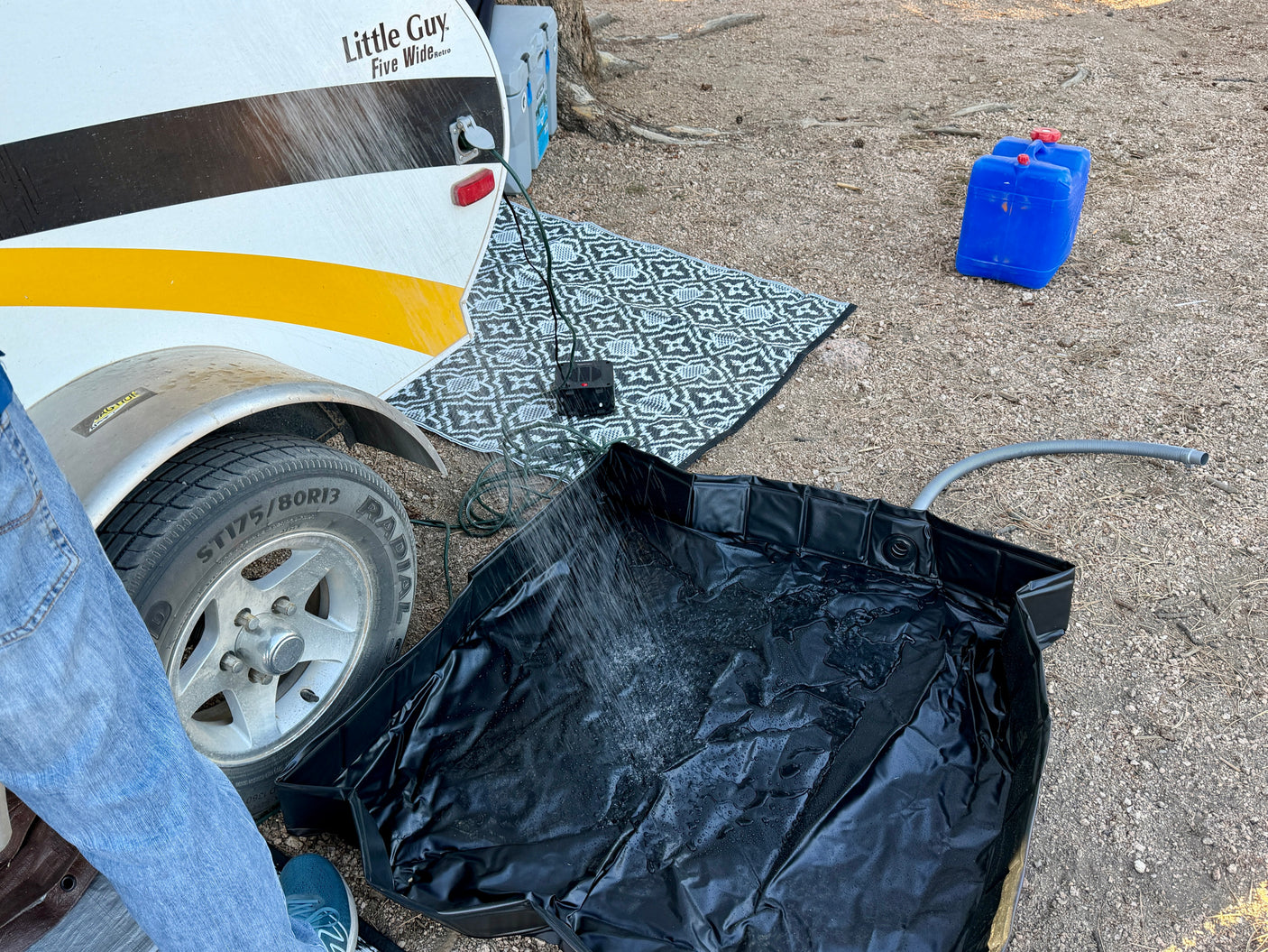 Camping with an **rv rental**: a teardrop trailer, outdoor shower spraying into a black basin, power unit, and water containers.