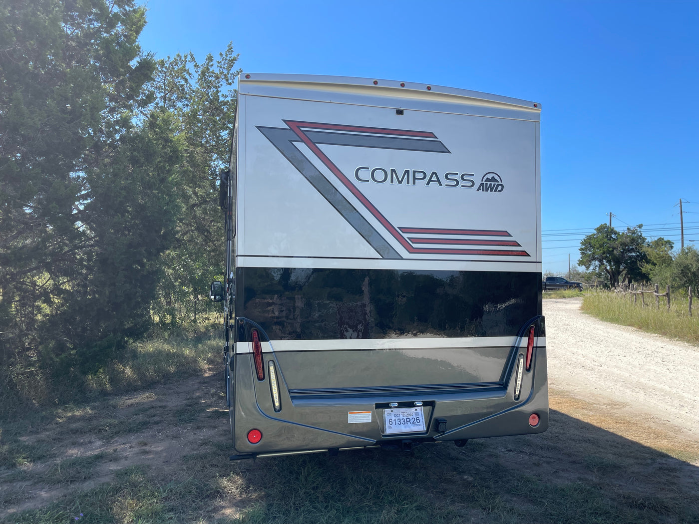 Rear view of a gray and white Compass AWD RV rental, a motorhome, parked on a dirt path next to trees. Perfect for your next trip. — photo 5