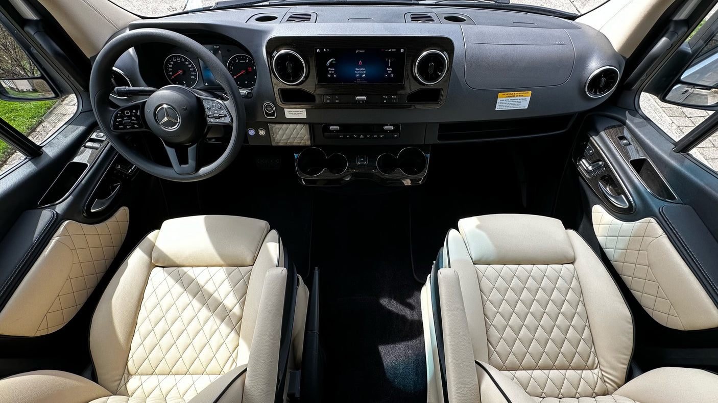 View inside a luxury RV rental, showing the driver's cockpit with Mercedes-Benz steering wheel, infotainment, and plush quilted seats.