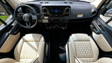 View inside a luxury RV rental, showing the driver's cockpit with Mercedes-Benz steering wheel, infotainment, and plush quilted seats.