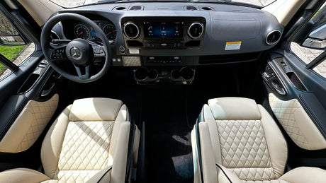 View inside a luxury RV rental, showing the driver's cockpit with Mercedes-Benz steering wheel, infotainment, and plush quilted seats.