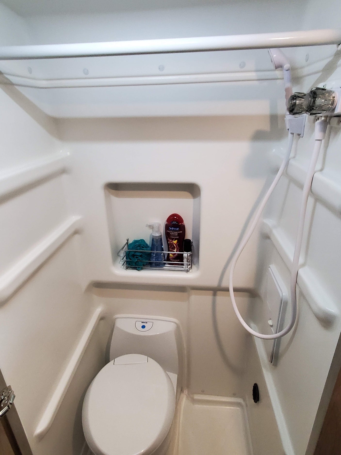 An RV rental's compact all-in-one bathroom unit, featuring a shower stall, toilet, and toiletries.