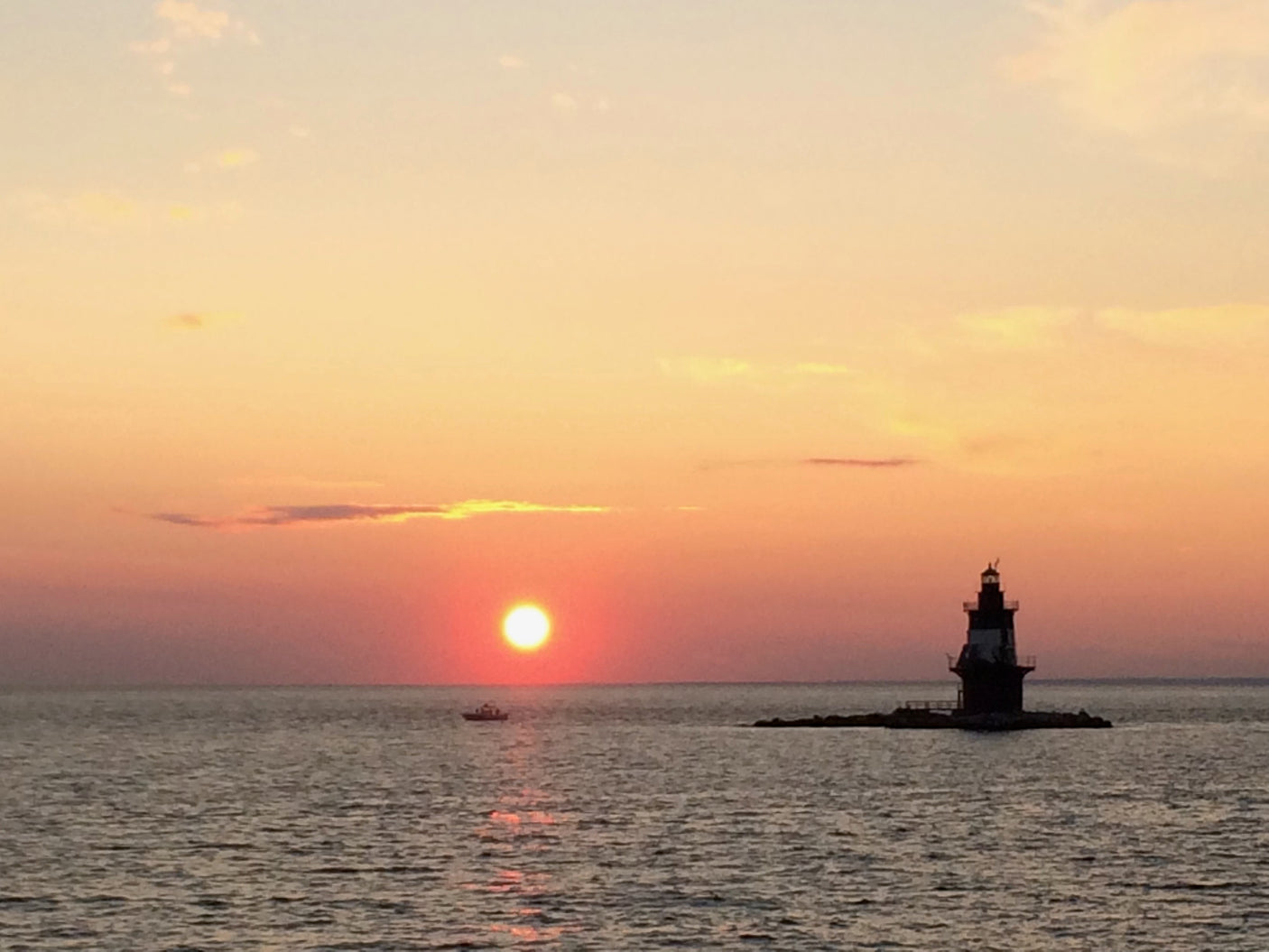 Breathtaking coastal sunset with a lighthouse and boat. An RV rental trip for serene ocean views awaits.