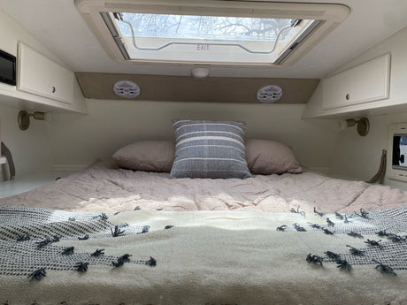 RV rental interior showing a snug bed with soft bedding, pillows, and an overhead exit skylight.