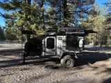 Rugged off-road expedition camping trailer in a sunny forest. Ideal RV rental for adventure.