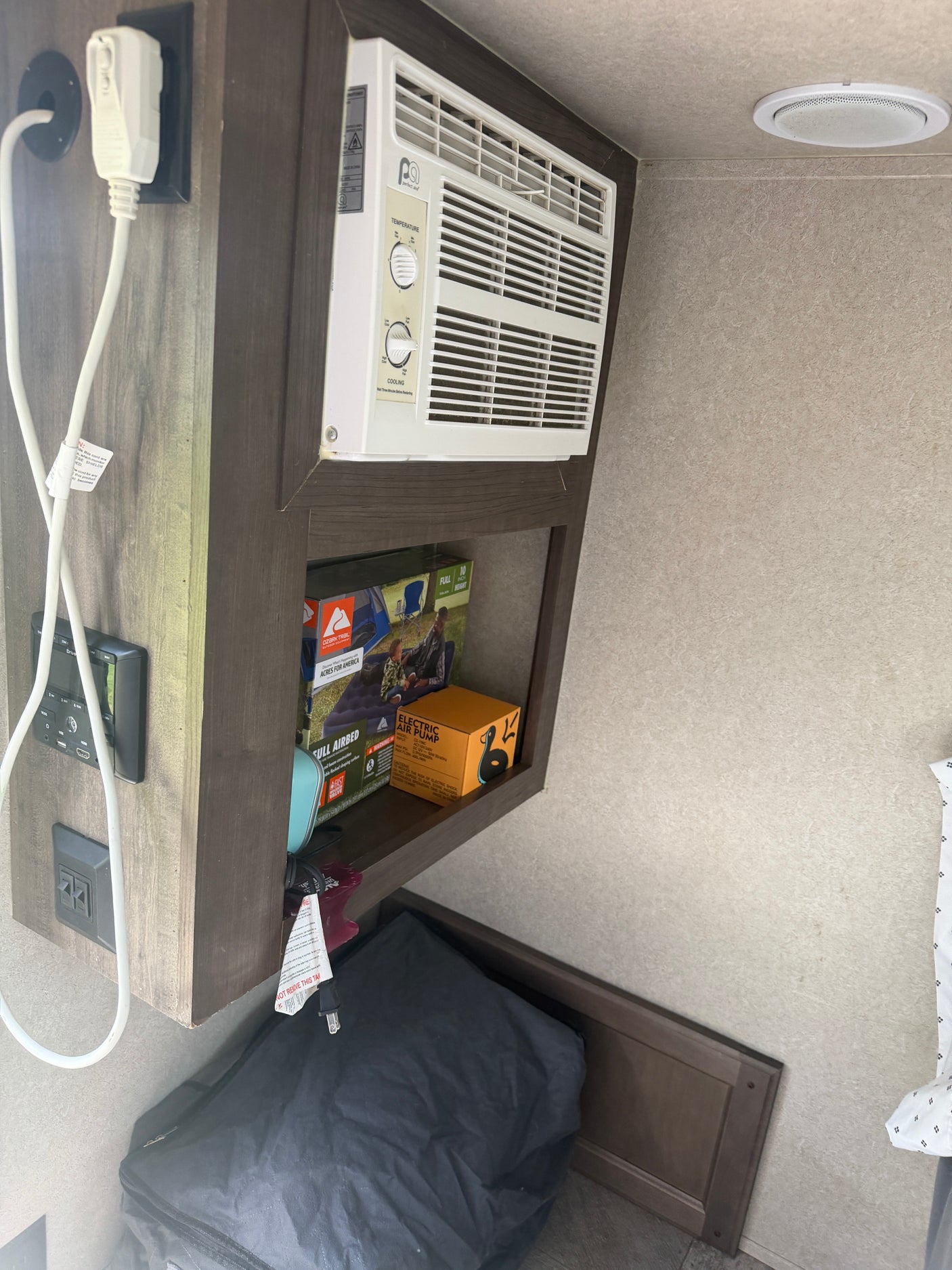 RV rental interior featuring a wall-mounted AC unit, power outlets, control panel, and shelved storage for camping gear.