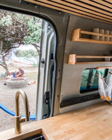 RV rental: wood counter, brass faucet inside, overlooking family by a fire pit on a sandy beach. Ideal camp life!