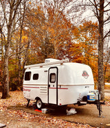 White Scamp RV rental parked at a vibrant autumn campsite, surrounded by fall foliage.