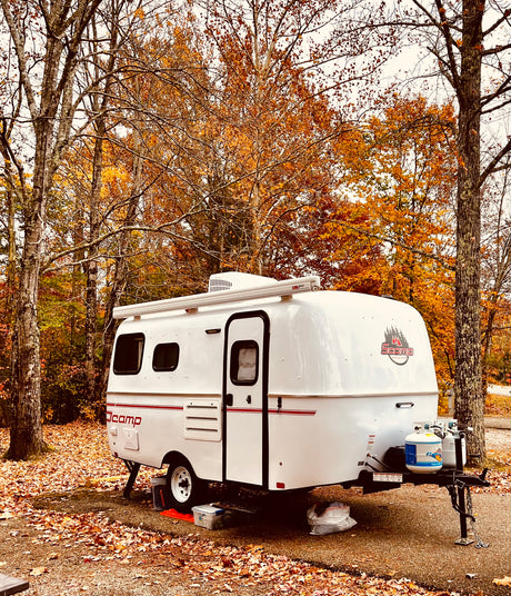White Scamp RV rental parked at a vibrant autumn campsite, surrounded by fall foliage.