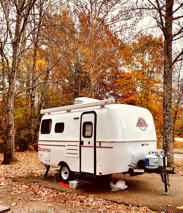 White Scamp RV rental parked at a vibrant autumn campsite, surrounded by fall foliage.