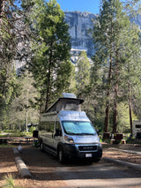 Silver camper van with pop-top at a scenic mountain campsite, ideal for an rv rental adventure.