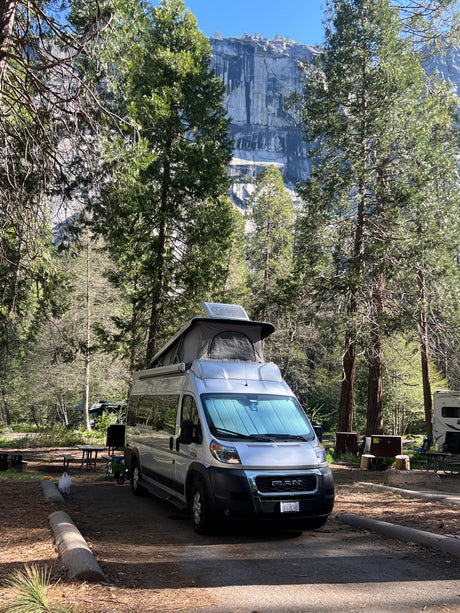 Silver camper van with pop-top at a scenic mountain campsite, ideal for an rv rental adventure.