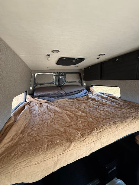 Inside an RV rental: a large, comfy bed with pillows, surrounded by textured walls & storage. Perfect for road trips.