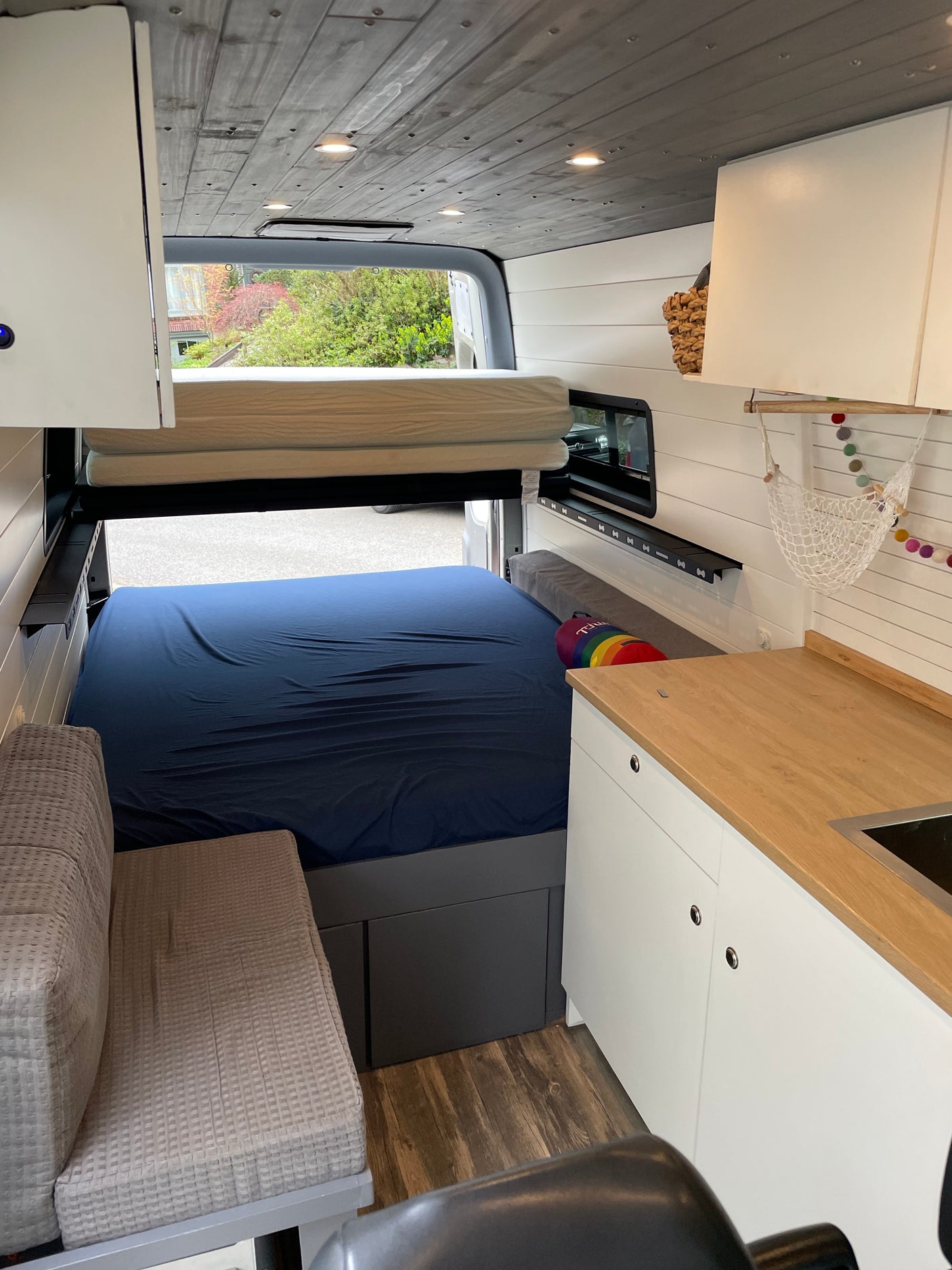 RV rental: Interior of a custom camper van with a bed, upper bunk, kitchenette, and bench seating.