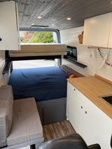 RV rental: Interior of a custom camper van with a bed, upper bunk, kitchenette, and bench seating.