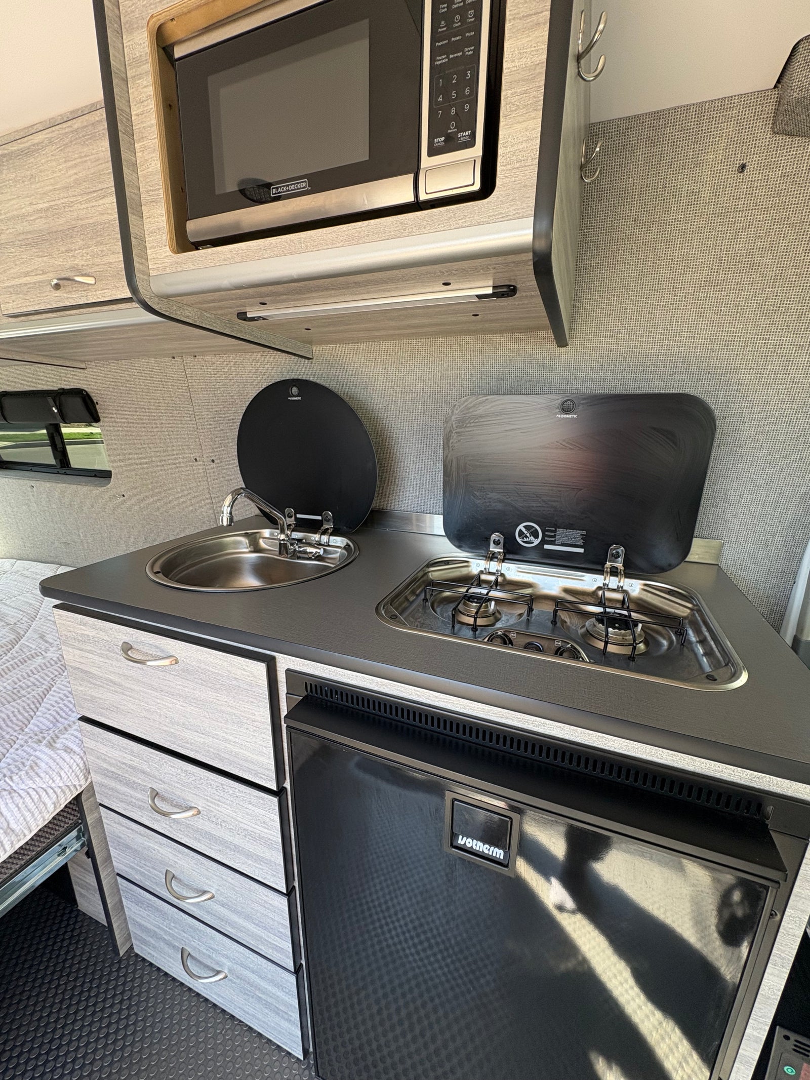 Inside this RV rental: a modern, compact kitchen with Black+Decker microwave, Dometic sink/stove, and Isotherm fridge.