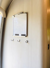RV rental interior: A practical whiteboard with marker and three hooks on a light wood-grain wall.