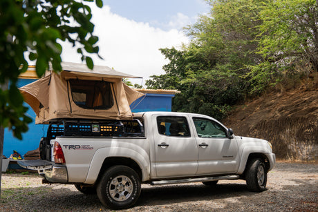 White Toyota Tacoma pickup truck with a tan rooftop tent, parked on gravel, for your next RV rental adventure.