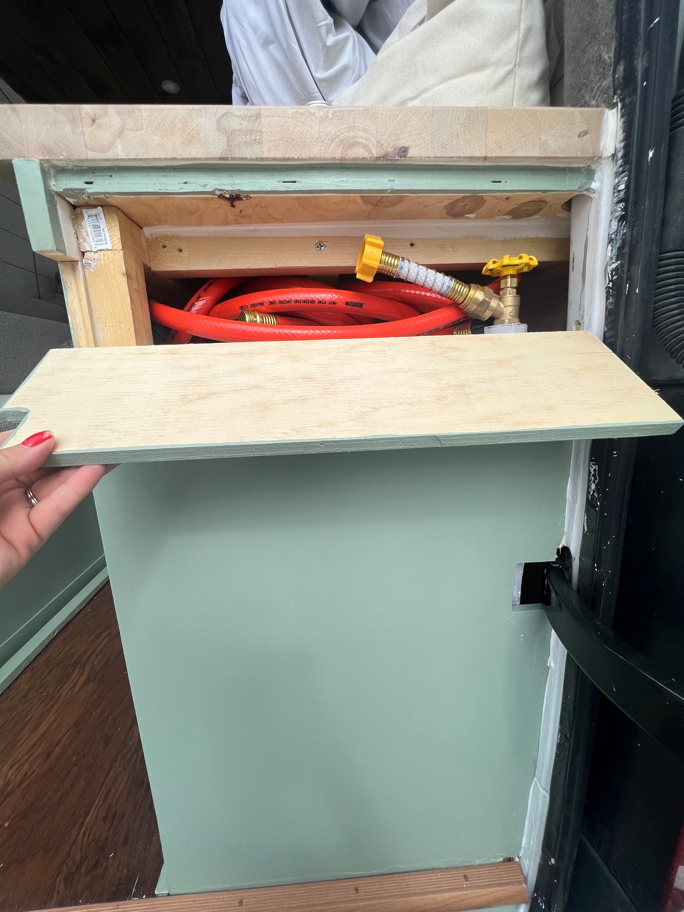 RV rental: This open storage compartment reveals an orange hose with a yellow valve inside a custom-built camper van cabinet.