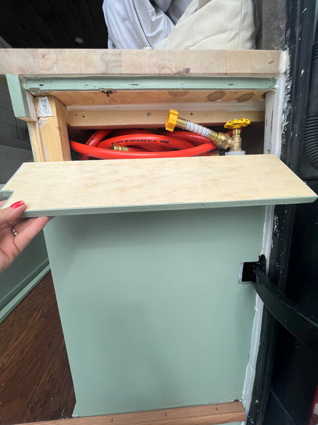 RV rental: This open storage compartment reveals an orange hose with a yellow valve inside a custom-built camper van cabinet.