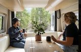 Couple enjoying coffee and forest views in their comfortable RV rental. Ideal for nature travel and cozy living.
