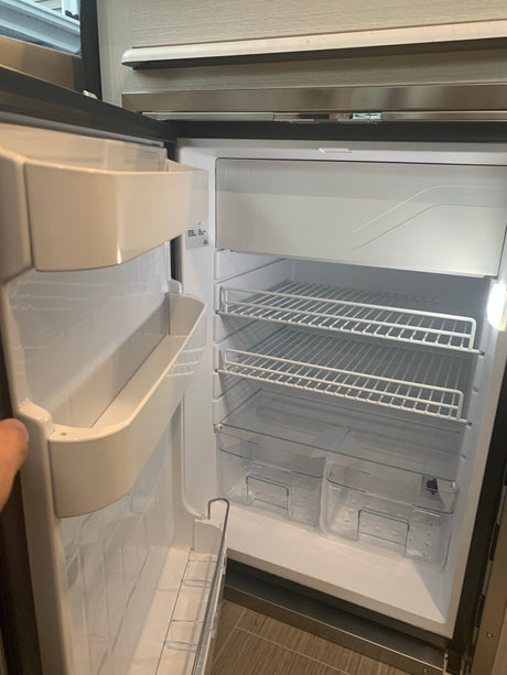 Open, empty refrigerator in an RV rental. Features white wire shelves, clear drawers, and door storage, ready for provisions.
