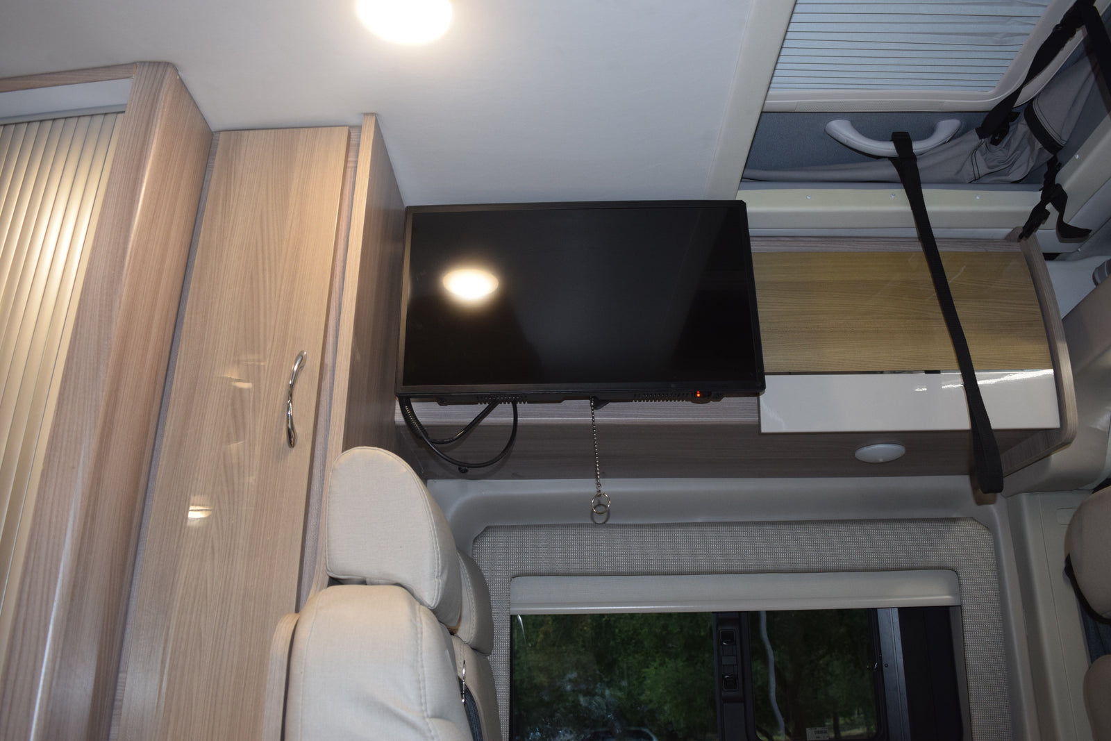 RV rental interior with a mounted TV, light wood cabinets, comfortable seating, and overhead storage.