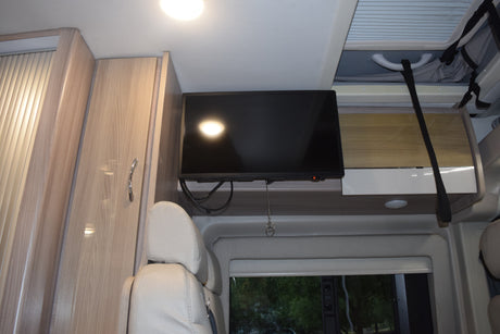 RV rental interior with a mounted TV, light wood cabinets, comfortable seating, and overhead storage.