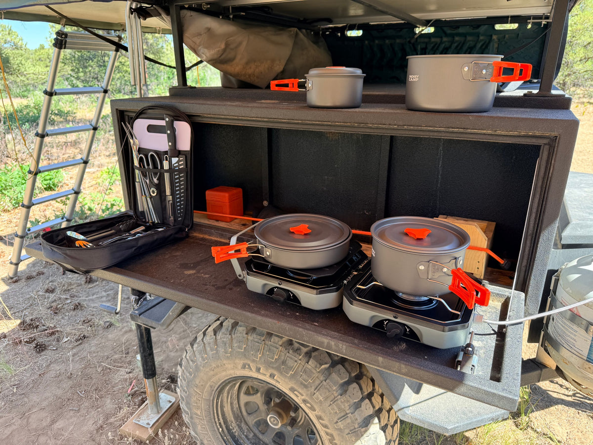  ideal for remote trips.|RV rental adventure: A camper trailer with an outdoor kitchen. A folding table with dinnerware and chairs are set for a meal.|rv rental camp kitchen setup on an overland trailer. Portable stoves & cookware ready for outdoor cooking — photo 4