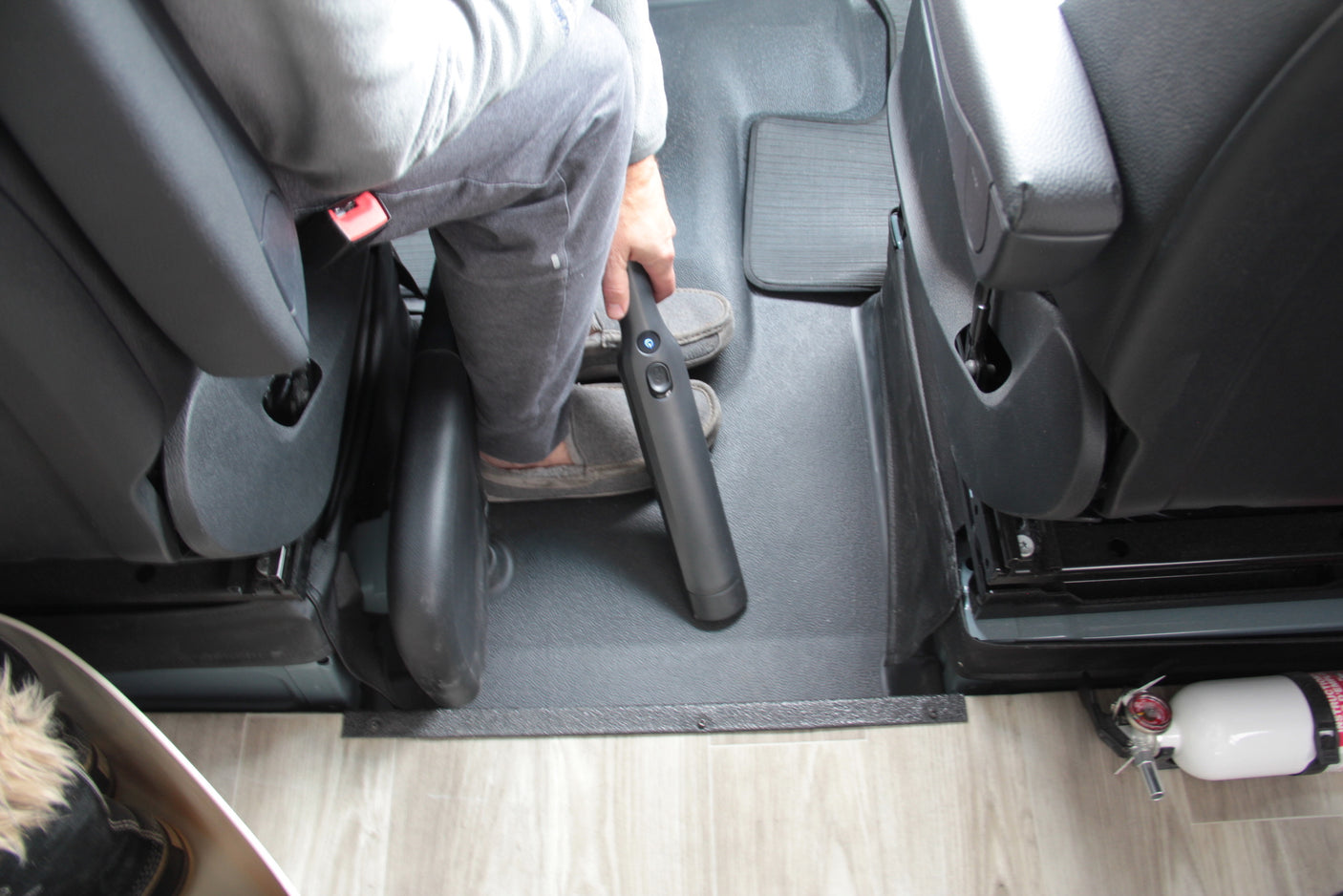 Inside an rv rental: passenger uses a handheld vacuum to clean the floor; fire extinguisher on right.