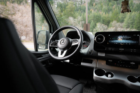 Interior of a modern Mercedes-Benz RV rental, showing the driver's seat, steering wheel, and dashboard display.