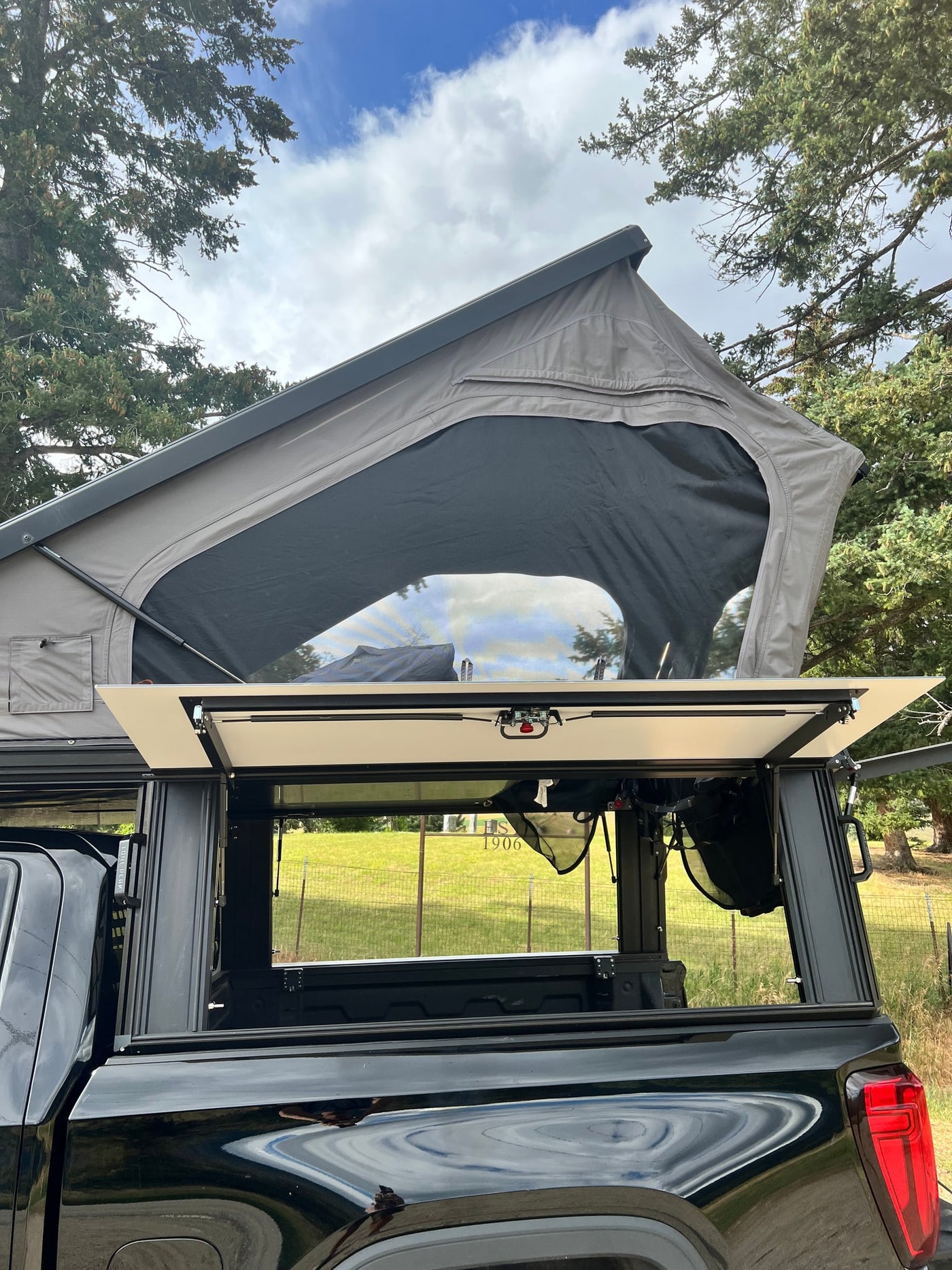 This rv rental showcases a black pickup truck with a deployed gray rooftop tent and open truck bed storage. Ideal for camping. — photo 16