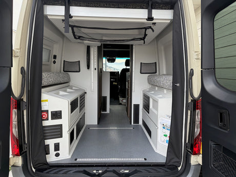 Open rear doors reveal a functional rv rental camper van interior with flexible seating and storage.
