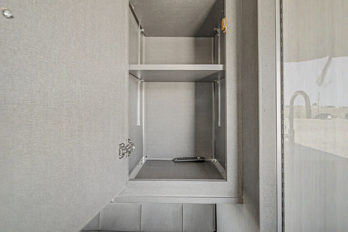Inside an RV rental: an open grey cabinet with adjustable shelves and a remote control, perfect for organized travel storage.