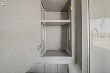 Inside an RV rental: an open grey cabinet with adjustable shelves and a remote control, perfect for organized travel storage.