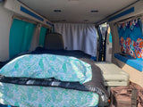 RV rental van interior: tropical bed, privacy curtain, and cooler for a comfortable mobile living.