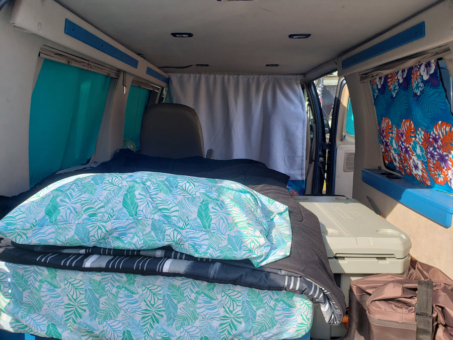RV rental van interior: tropical bed, privacy curtain, and cooler for a comfortable mobile living.